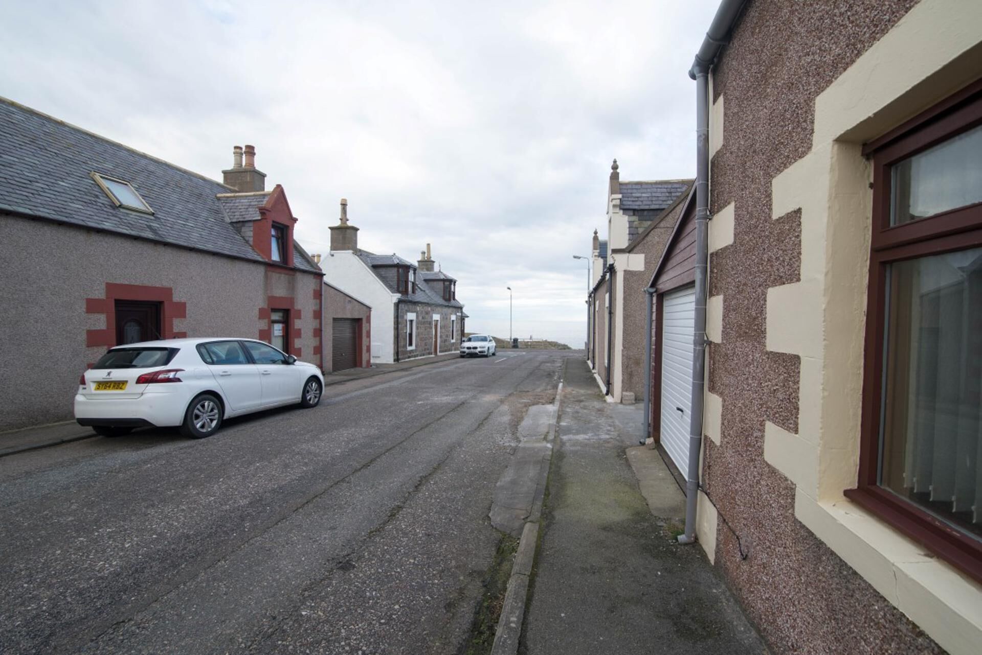 A narrow street lined with residential buildings, featuring a white car parked on the left.