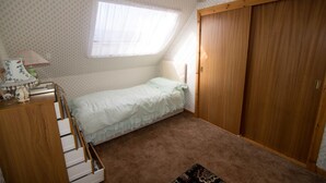 A small bedroom with a single bed, a wooden wardrobe, a desk with a lamp, and a window with sheer curtains. - Come Along and Enjoy the Beautiful Moray Coast (Buckie)