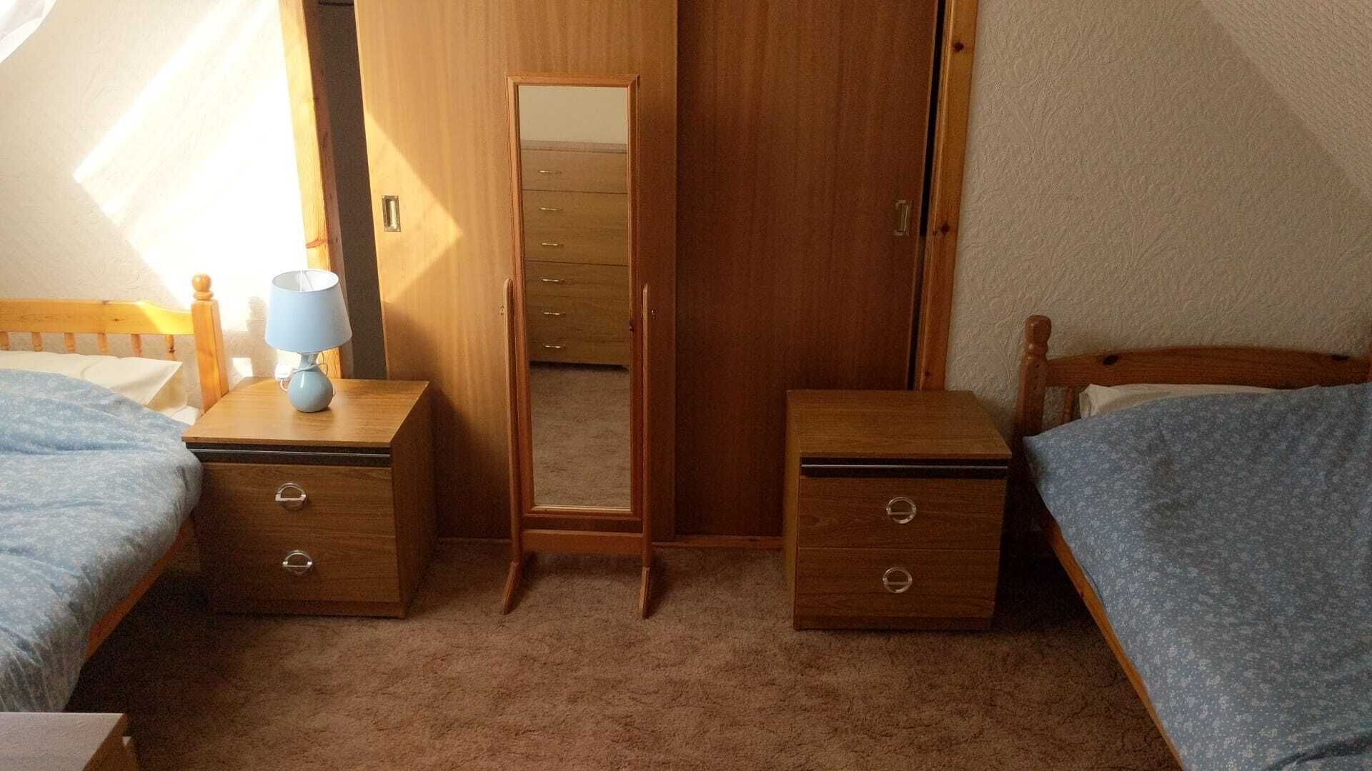 Un dormitorio con dos camas individuales, un armario de madera, un espejo y una mesita de noche con una lámpara.