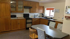 A kitchen with wooden cabinets, a microwave, stove, and a dining table with chairs. - Come Along and Enjoy the Beautiful Moray Coast (Buckie)