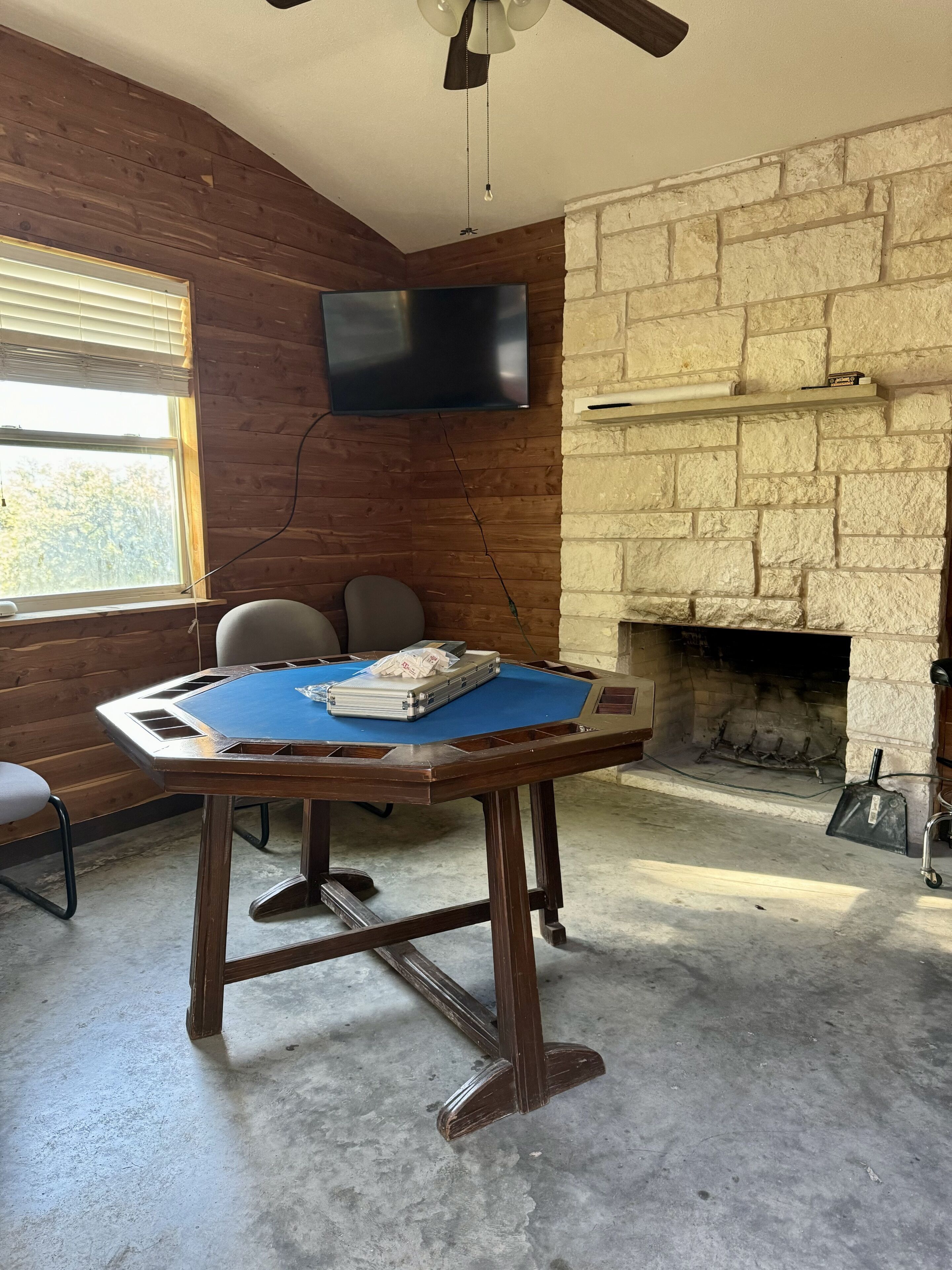A room with a pool table, a television mounted on the wall, a fireplace, and a window with blinds.