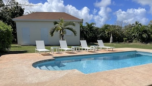 Une piscine bordée de chaises longues blanches, avec un palmier en arrière-plan.