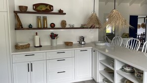 Une cuisine moderne avec des meubles blancs, des étagères en bois et un coin repas avec des chaises blanches.