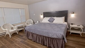 A bedroom with a large bed, two white wicker chairs, a nightstand with a phone, and a window with blinds. - Prairie Voyager  (Prairie Du Chien)