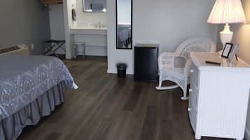 Et soveværelse med seng, skrivebord med lampe, stol, en lille skraldespand og et spejl på væggen.