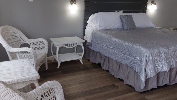 A bedroom with a bed, two white wicker chairs, a small white table, and a wooden floor. - Prairie Voyager  (Prairie Du Chien)