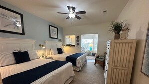 Een slaapkamer met twee bedden, een plafondventilator, een kaptafel en een bankje.