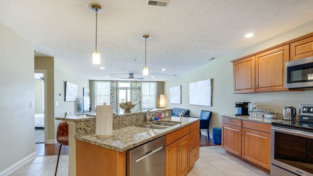A modern kitchen with granite countertops, stainless steel appliances, wooden cabinets, and pendant lighting. - Downtown St Joseph Condo w/ Balcony & Harbor View (St Joseph)