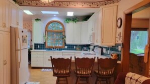 A kitchen with white cabinets, a wooden dining table with chairs, and a red armchair. - Victoria House luxurious country feel. Close to Buffalo Bills stadium. (Elma Center)