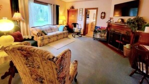 A cozy living room with a sofa, armchairs, a fireplace, and a television. - Victoria House luxurious country feel. Close to Buffalo Bills stadium. (Elma Center)