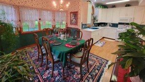 A dining area with a table set for four, surrounded by wooden chairs. There is a chandelier above the table, and the room has a floral-patterned carpet. - Victoria House luxurious country feel. Close to Buffalo Bills stadium. (Elma Center)