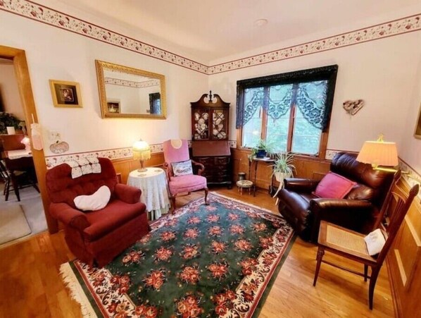 A traditional living room with a floral rug, two armchairs, a sofa, a small table, and a fireplace.
