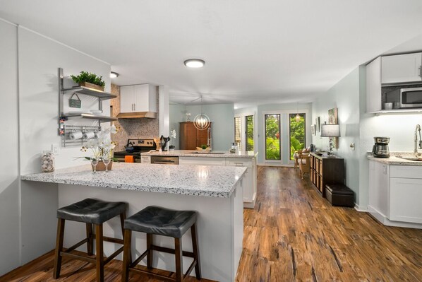 A modern kitchen with a central island, wooden flooring, and a view of the outdoors.