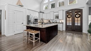 A spacious kitchen with a large island, white cabinetry, and a dark wooden door with wreaths. - Enjoy luxury Sunsets at the Lake! (SEVIERVILLE)
