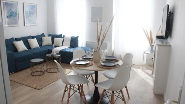A modern living room with a blue sofa, white chairs, a round dining table set for four, and a small coffee table. - L'amiral Centre Ville Balnéo Parking (Grasse)