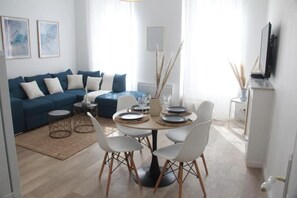 Un soggiorno moderno con un divano blu, sedie bianche, un tavolo da pranzo rotondo apparecchiato per quattro persone e un tavolino da caffè.
