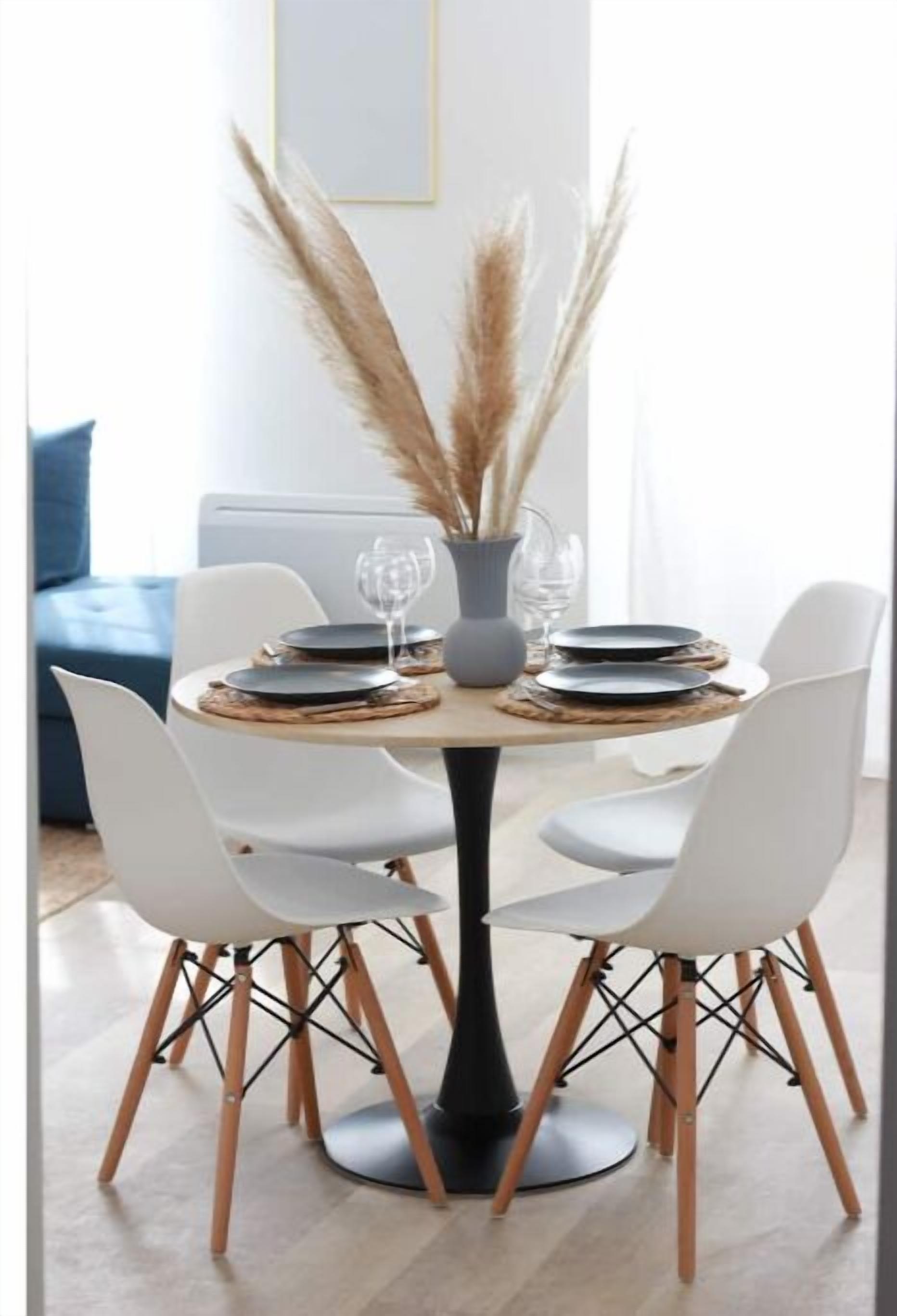 A round dining table with white chairs and a vase of pampas grass.