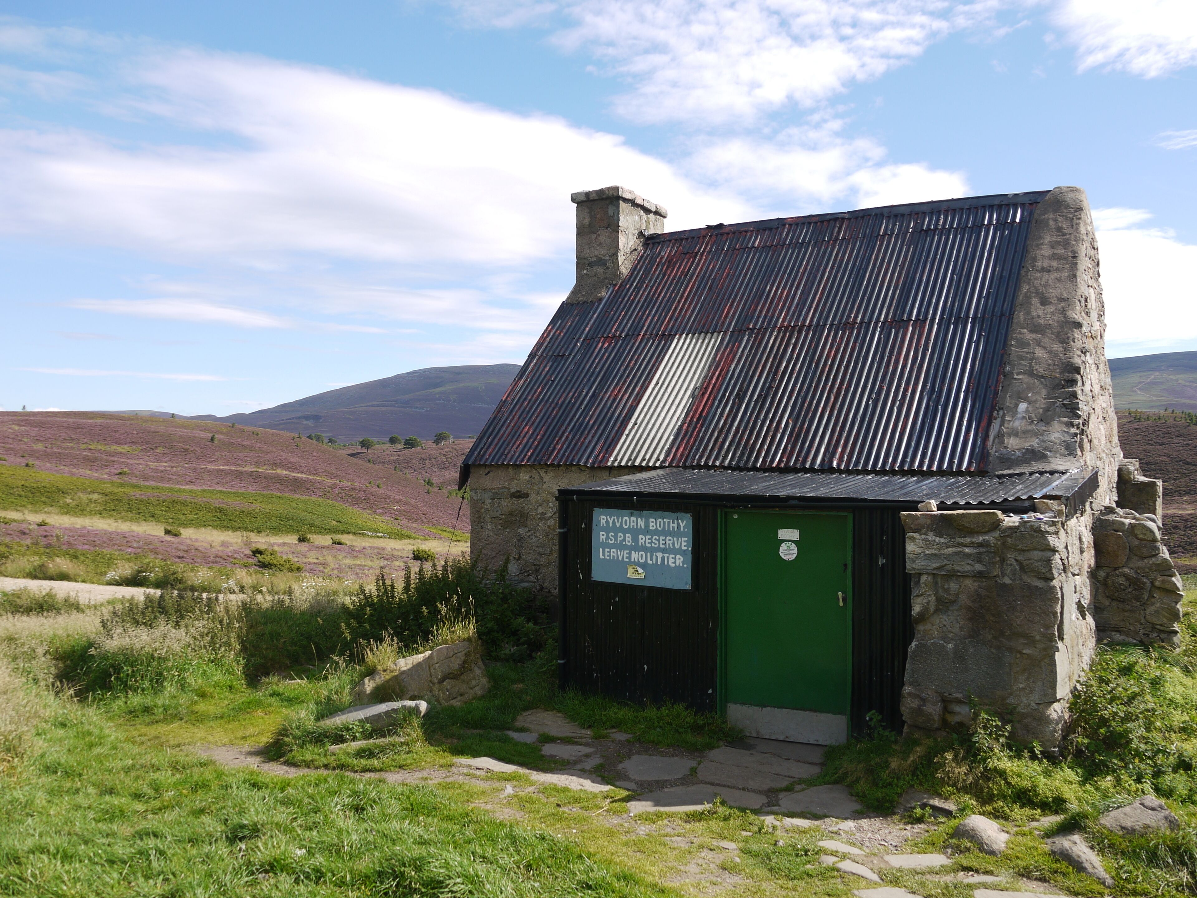A stone building with a green door and a sign that reads "RYVORN BOTHY R.S. RESERVE LEAVE NO LITTER."
