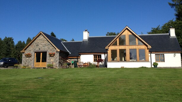 A two-story house with a stone exterior and a large wooden front porch. - SECLUDED COTTAGE IN THE VERY HEART OF THE HIGHLANDS OF SCOTLAND (Kingussie)