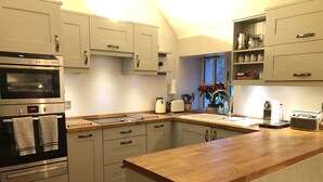 A kitchen with light-colored cabinets, a built-in oven, a wooden countertop, and a window with a view of trees. - SECLUDED COTTAGE IN THE VERY HEART OF THE HIGHLANDS OF SCOTLAND (Kingussie)