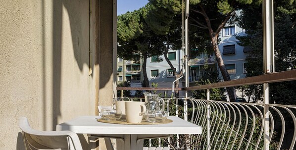 A balcony with a table, chairs, a pitcher, and a potted plant.