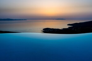 A coastal landscape with a calm sea, distant landforms, and a clear sky. - ALOS RESIDENCE (Tinos)