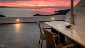 En terrasse med et bord og stole med udsigt over en solnedgang over havet.