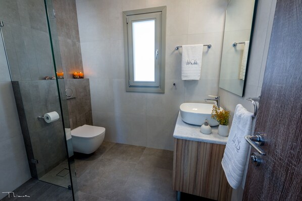 Une salle de bain moderne avec une douche à parois de verre, des toilettes, un lavabo avec un miroir et une fenêtre.