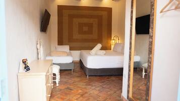 Habitación de hotel con una cama grande, una cama más pequeña, un escritorio y un aparador. Hay un espejo grande en la pared y un televisor montado sobre la cama.
