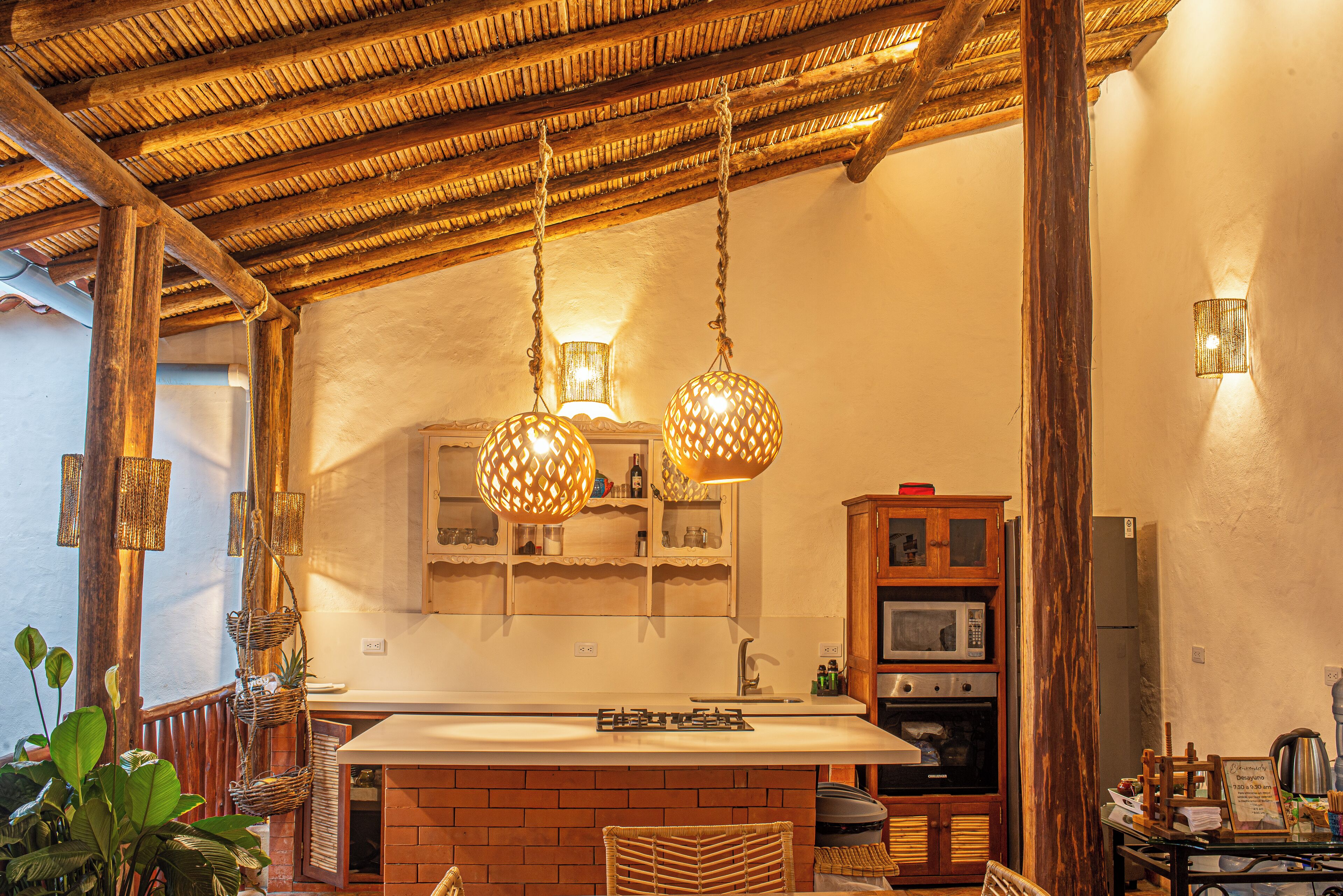 A rustic kitchen with a brick island, hanging wicker chandeliers, wooden cabinets, and a built-in oven.