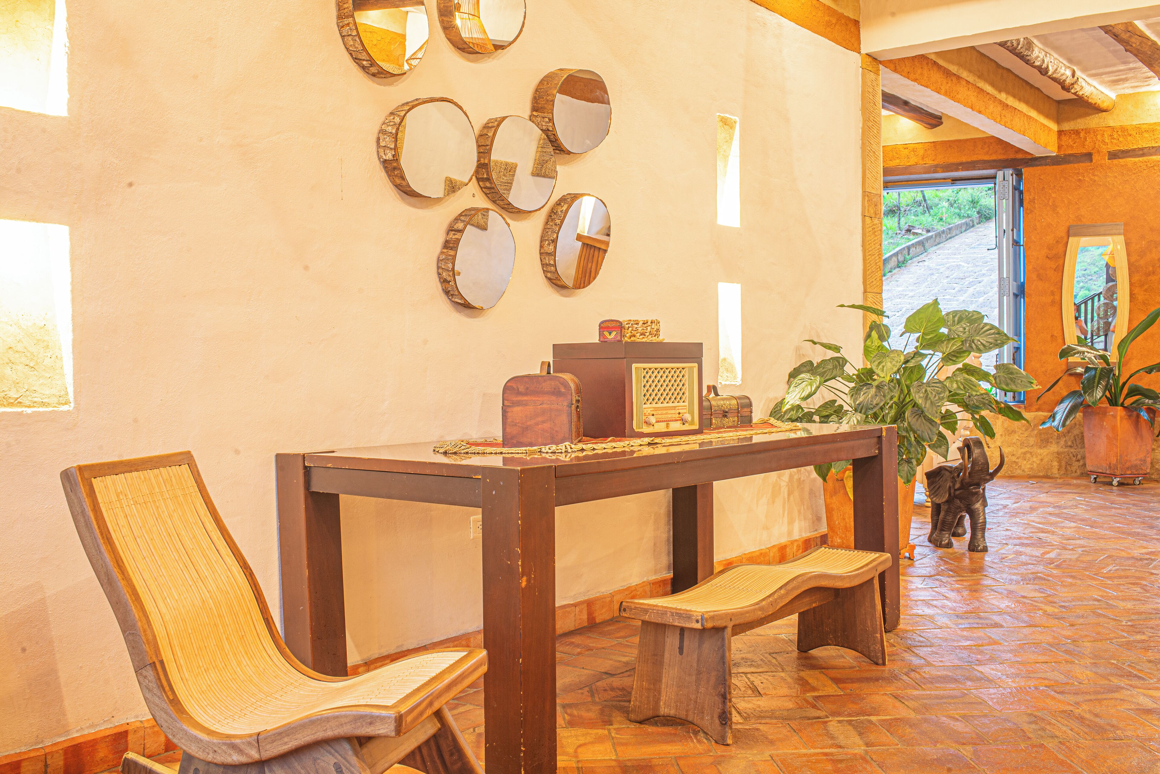 A wooden dining table with benches, surrounded by mirrors and potted plants.