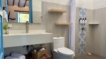 Un baño moderno con un lavamanos grande, inodoro y zona de ducha. Hay repisas sobre el lavamanos y una cesta con toallas en el suelo.