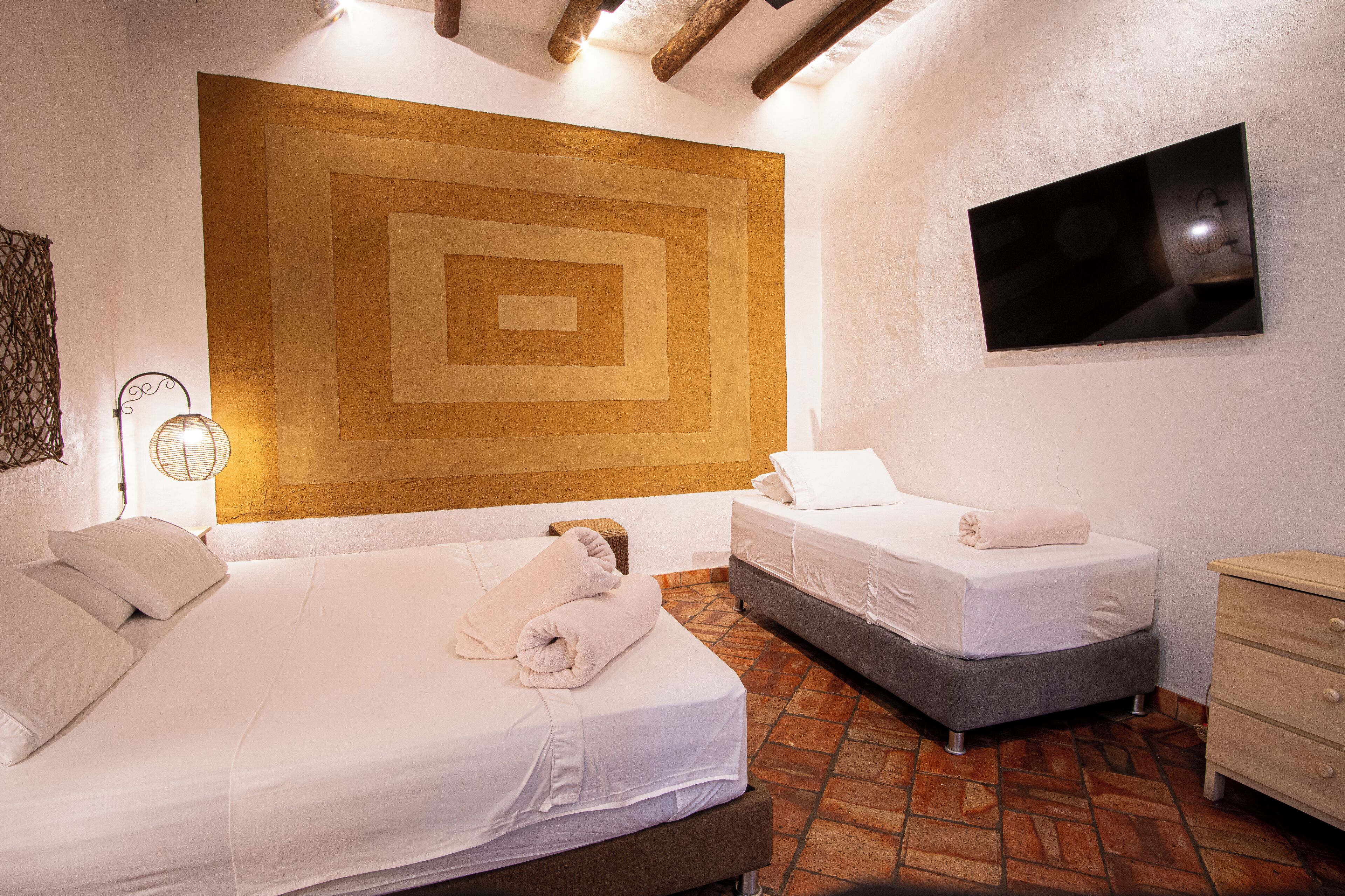 Habitación de hotel con dos camas, una obra de arte grande en la pared, un televisor de pantalla plana y techo de madera.