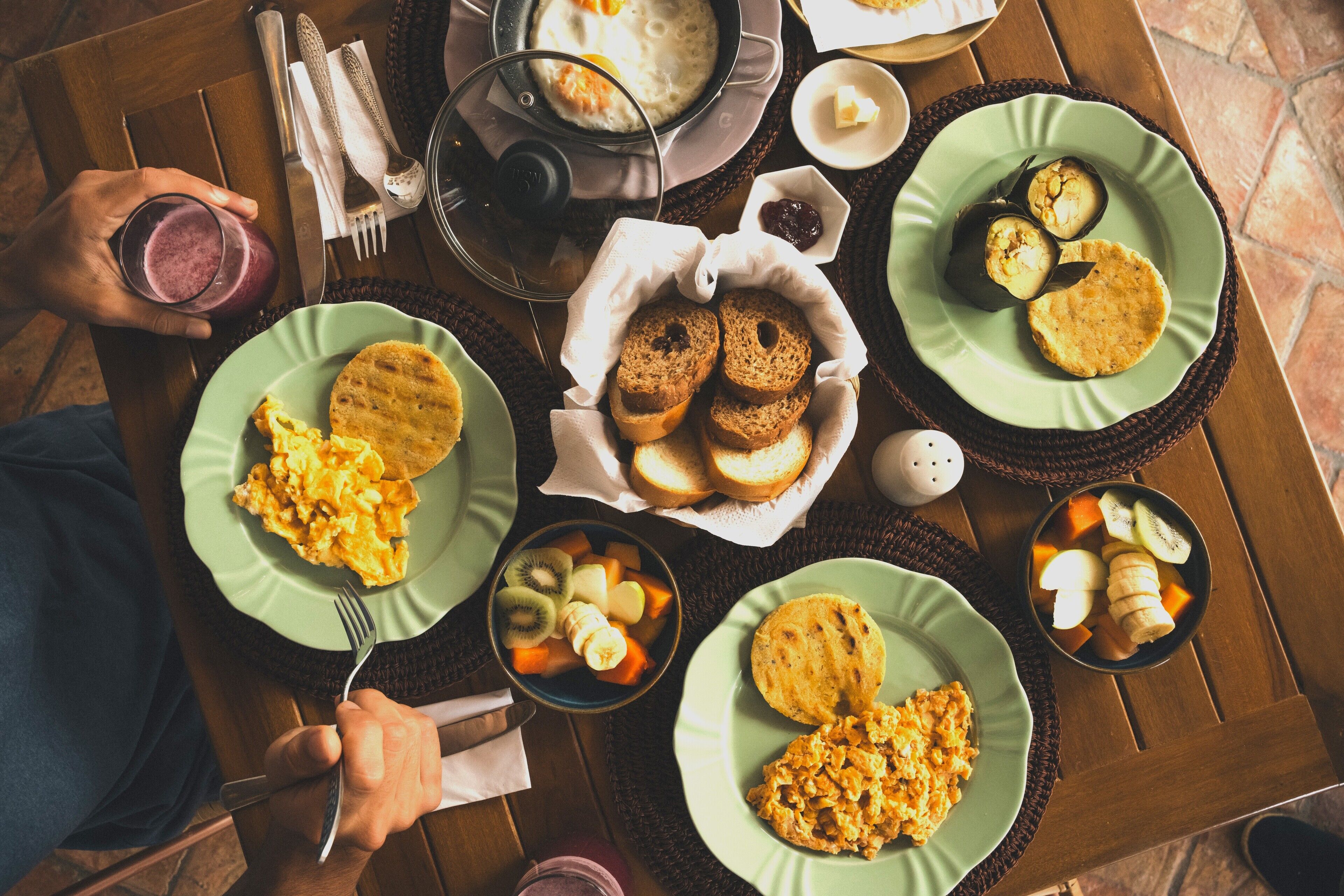 A breakfast table with plates of scrambled eggs, toast, and fruit.