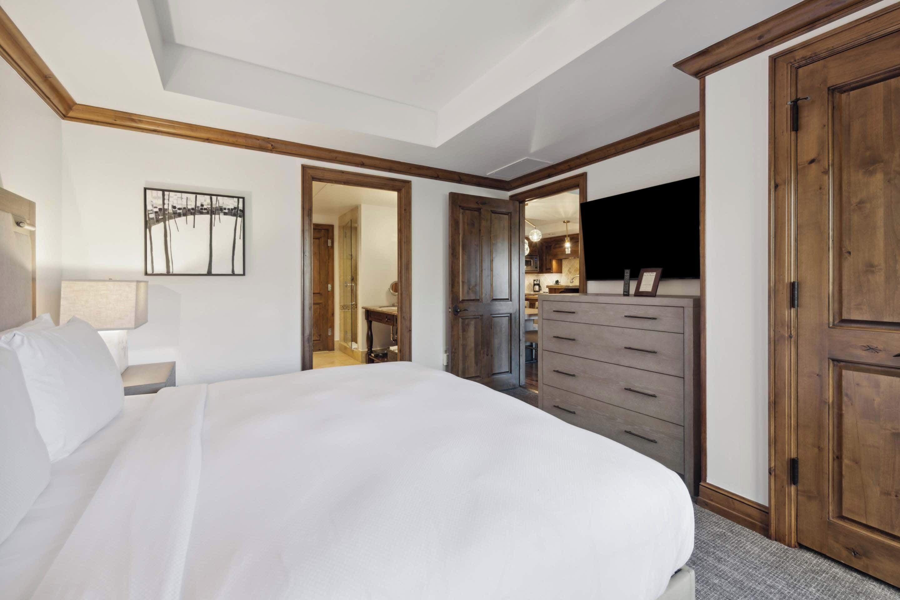 A hotel room with a large bed, wooden wardrobe, a mirror, and a television.