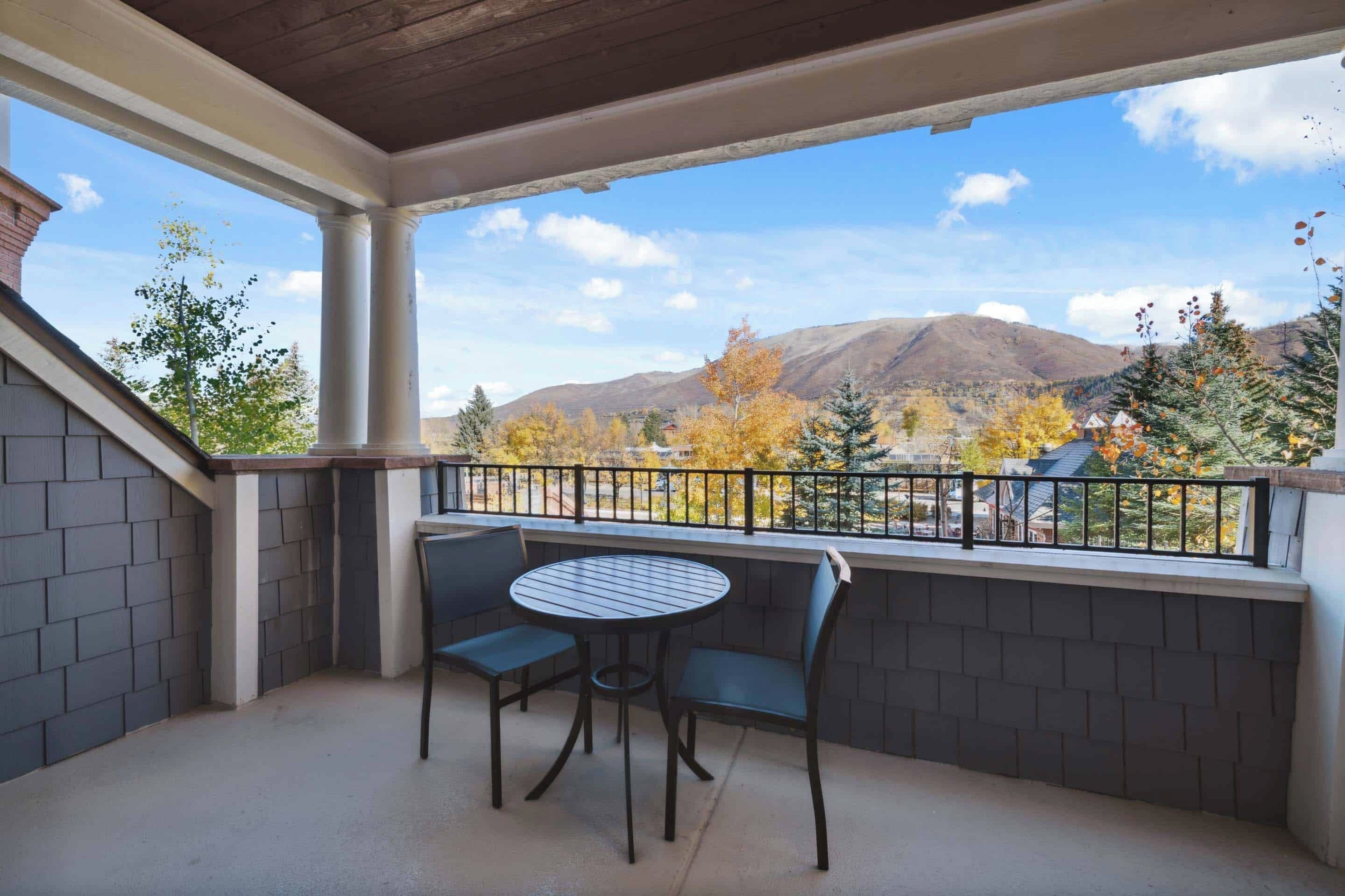 Un balcón techado con mesa y sillas, con vistas a un paisaje montañoso con follaje otoñal.