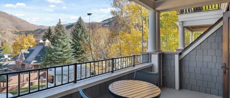 A balcony with a table and chairs, overlooking a mountainous landscape with autumn foliage.