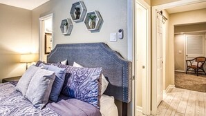 Ein Schlafzimmer mit einem Bett, einem Nachttisch, einer Wandleuchte und einer Tür zu einem anderen Raum.