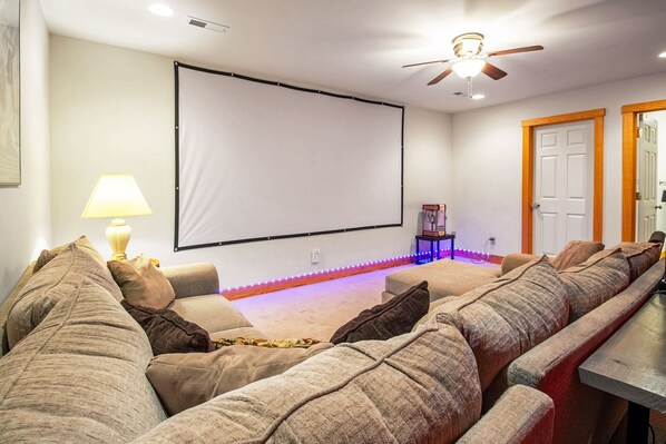 A home theater room with a large screen, comfortable seating, and a ceiling fan.