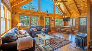 A spacious cabin with a high ceiling, large windows, a cozy living area with a sofa and coffee table, a dining table, and a wood stove. - Hot tub, Firepit, Beautiful Mountain Views! (Stanardsville)