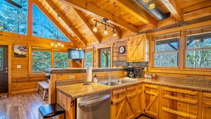 A wooden cabin kitchen with a large island, wooden cabinets, and a clock on the wall. - Hot tub, Firepit, Beautiful Mountain Views! (Stanardsville)