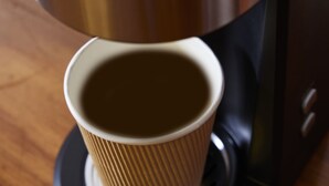 Una cafetera con una taza de papel en su base.