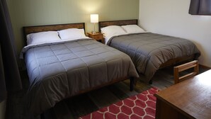 Una habitación con dos camas, una mesita de noche con lámpara y una mesa de madera.