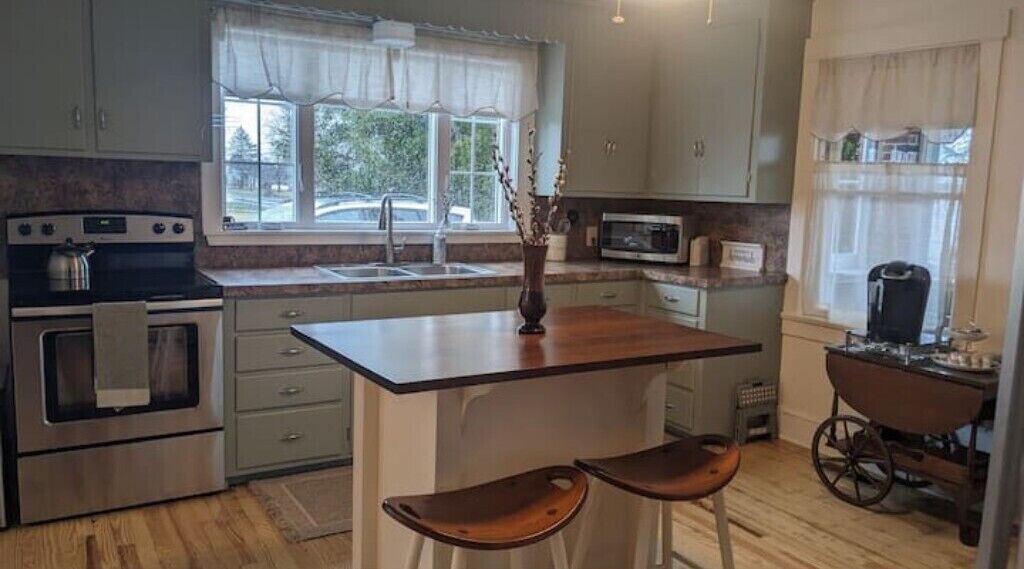A kitchen with a central island, stainless steel appliances, and a window with curtains.