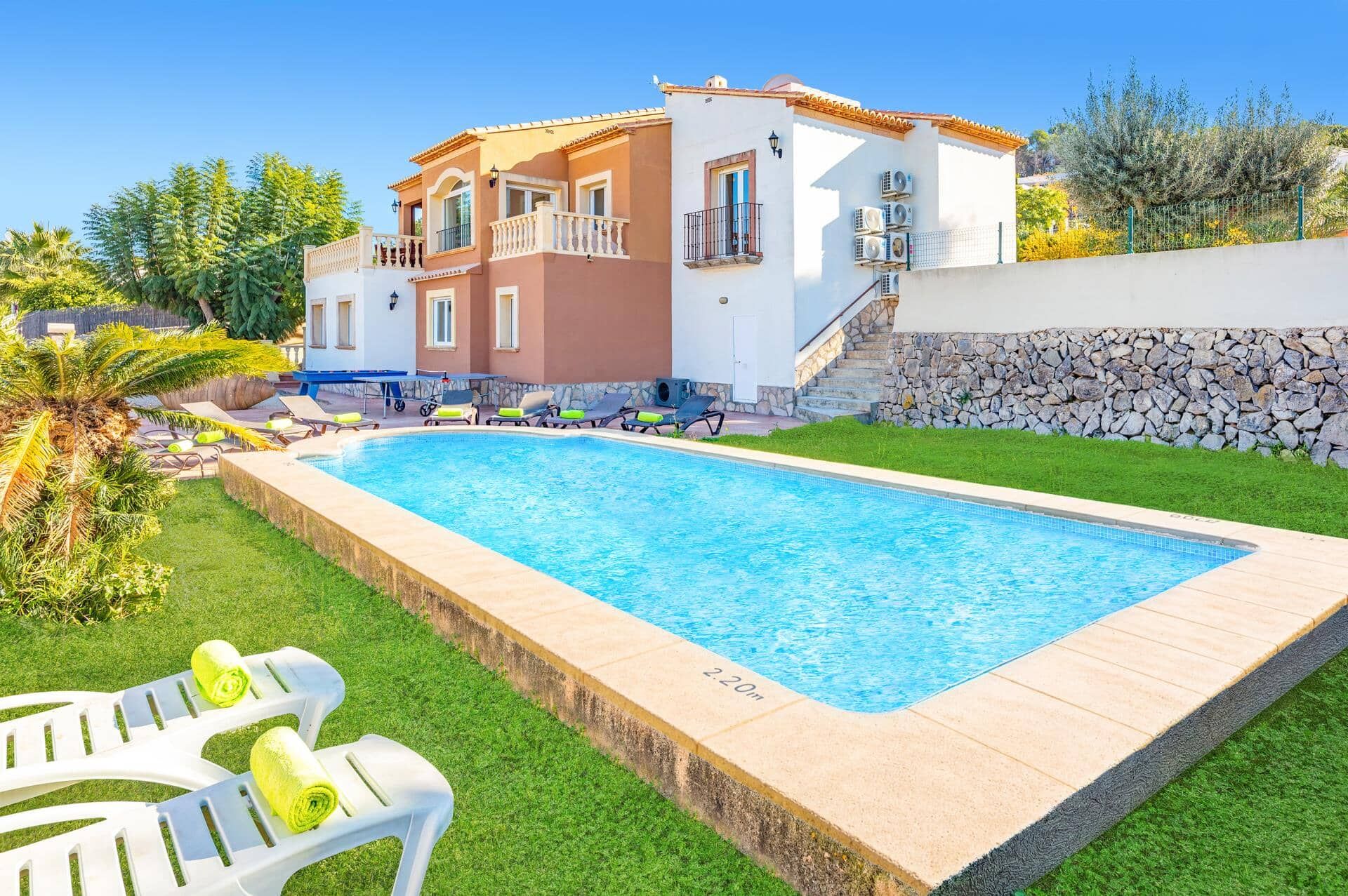 A two-story house with a swimming pool, stone wall, and a well-maintained lawn.