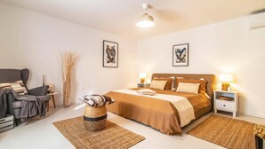 Une chambre à coucher comprenant un lit, deux tables de chevet avec des lampes, une chaise et deux œuvres d’art accrochées au mur.