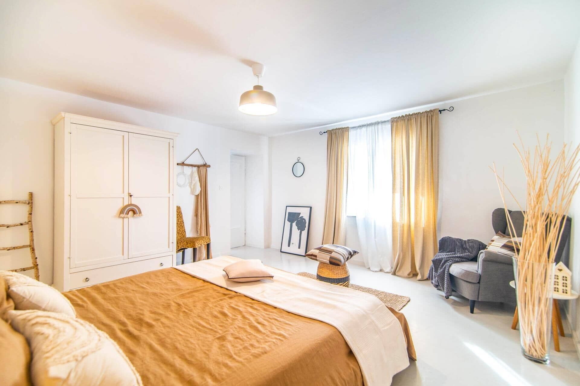 Ein Schlafzimmer mit Bett, Kleiderschrank, Spiegel, Stuhl und einem kleinen Tisch mit Lampe.