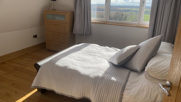 Une chambre à coucher avec un lit, une table de chevet, une fenêtre avec des rideaux et une vue sur la campagne.