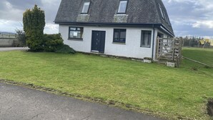 Une maison de plain-pied avec un toit sombre, des murs extérieurs blancs et un petit jardin à l’avant.