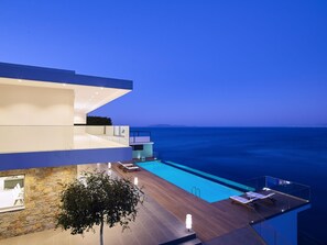 A modern building with a pool, a view of the sea, and a dining area.